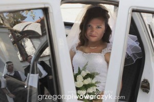 Panna młoda przed kościołem siedzi jeszcze w samochodzie trzymając w ręku piękny bukiet ślubny.